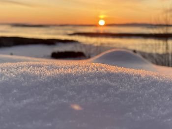 Surface level of snow on land against sky during sunset