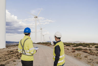 Technicians discussing on road looking at wind turbines at wind farm