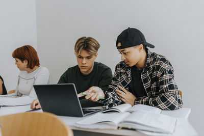 Male students using laptop together at desk in classroom