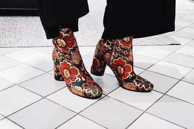 Low section of woman wearing floral patterned shoes while standing on tiled floor