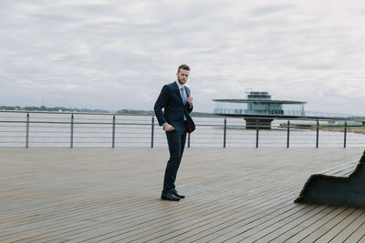 Full length portrait of young man standing on railing against sky