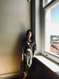 Portrait of young woman standing by window at home