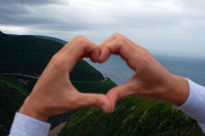 Cropped hands making heart shape against mountain