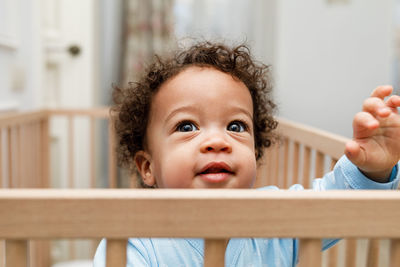 Cute baby boy looking away in crib at home