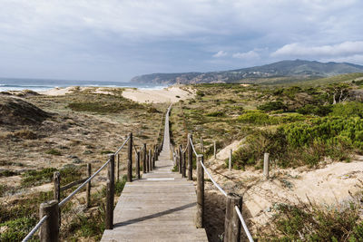 Empty, wooden boardwalk on a beach praia do guincho in sintra. view of grass and sand with hills