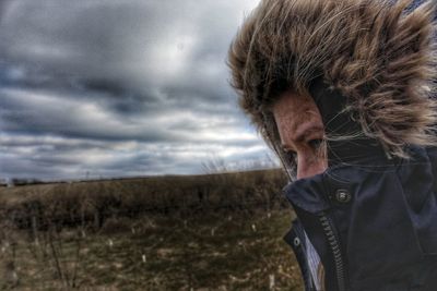 Close-up of woman in hooded jacket against cloudy sky