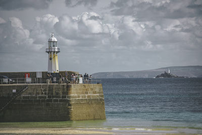 People standing by lighthouse against cloudy sky