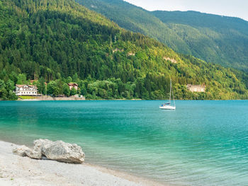 Stones on shore of blue green water of mountain lake molveno at foot of the brenta dolomites, italy.