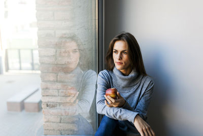 Young woman eating an apple at a window