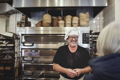 Smiling senior male baker standing against cooling rack at bakery