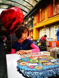 Thoughtful girl sitting by red balloon at desk