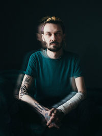 Portrait of young man sitting against black background