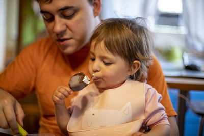 Girl eating ice cream while sitting with father at home