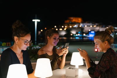 Friends sitting on illuminated smart phone in city at night