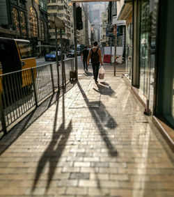 Rear view of woman walking on sidewalk in city