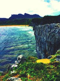 Scenic view of sea by mountain against sky