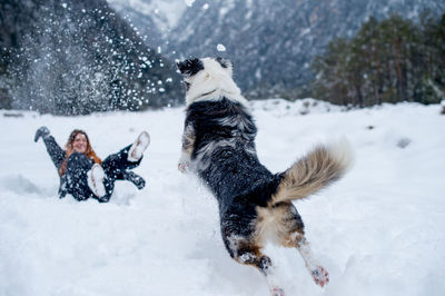 Cheerful woman playing with dog on snow covered field