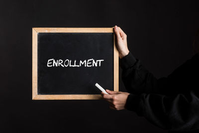 Cropped hand holding blackboard against black background