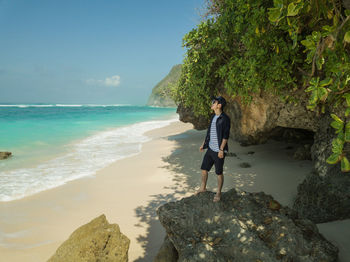 Man standing on rock at beach against sky