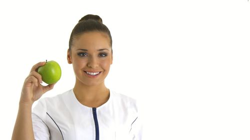 Portrait of smiling woman holding apple against white background
