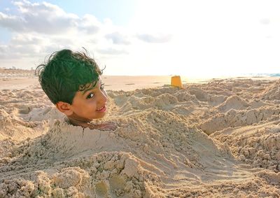 Portrait of boy in sand on beach against sky