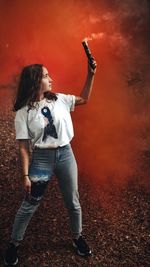 Full length of young woman holding distress flare outdoors