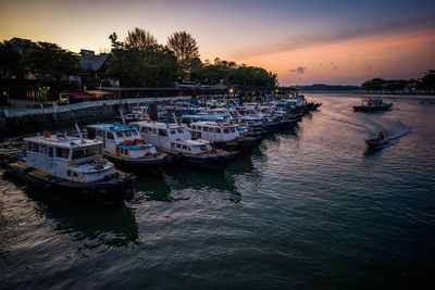 Boats moored in harbor at sunset