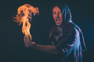 Portrait of shouting man holding fire against black background