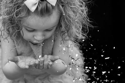 Close-up of cute girl holding glitter in hands against black background