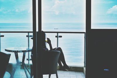 Woman on chair in balcony seen through glass against sea