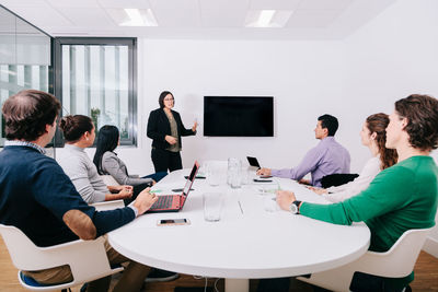 Mature woman explaining in seminar while male and female colleagues sitting by conference table at workplace