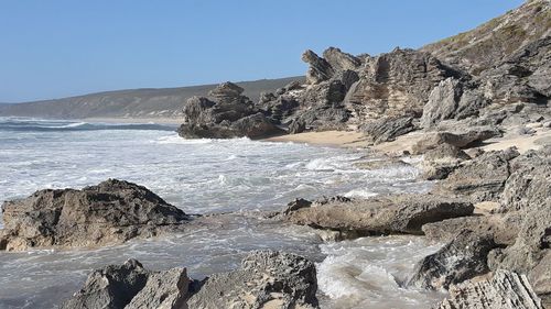 Scenic view of rocks on beach against clear sky