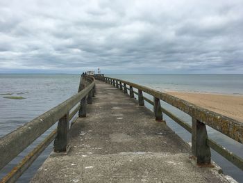 View of pier leading to calm sea against cloudy sky