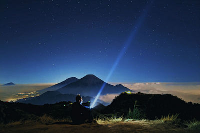 Silhouette man sitting on land against sky at night