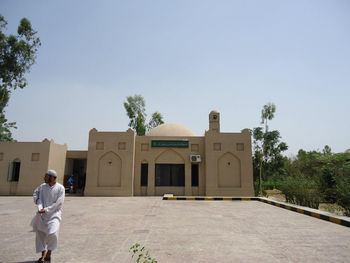 Rear view of man standing by building against sky