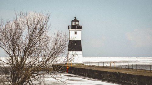 Lighthouse amidst buildings against sky during winter