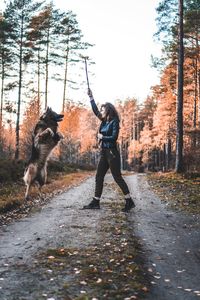 Woman holding stick with dog on field against sky