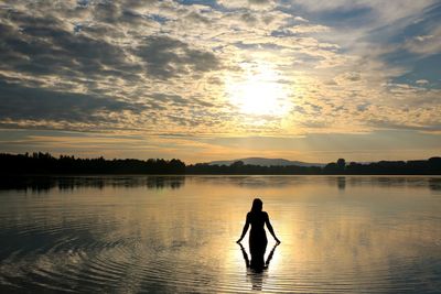 Silhouette man in lake against sky during sunset