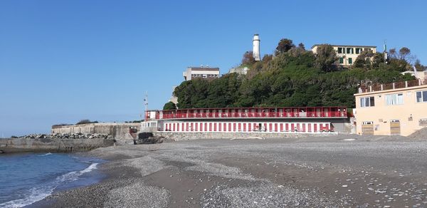 Buildings by sea against clear blue sky