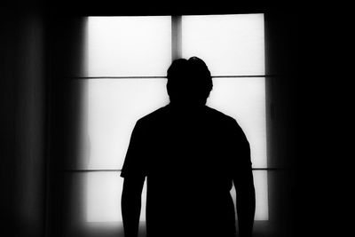 Rear view of silhouette man standing against window