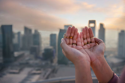 Midsection of person holding cityscape against sky during sunset