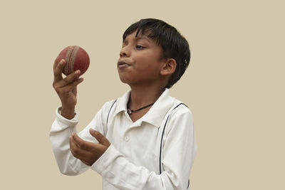Portrait of boy holding ball against gray background