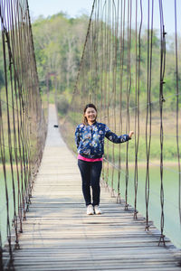 Full length portrait of woman standing on footbridge against sky