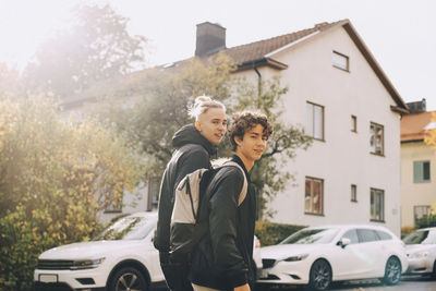 Portrait of smiling male friends walking together against house and cars in city