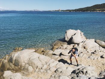 Man on rock by sea against sky