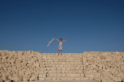 Woman with arms outstretched standing on steps against clear blue sky