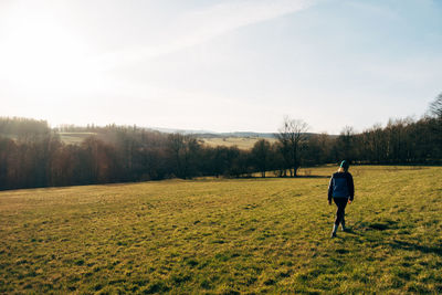 Rear view of man walking on field against sky
