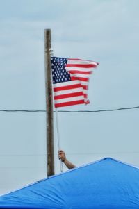 Cropped hand holding american flag on top of roof against clear sky