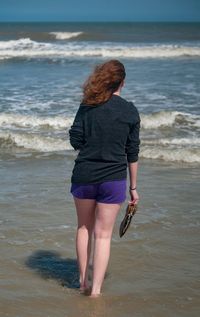 Rear view of teenage girl standing on shore in sea