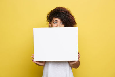 Portrait of woman holding blank paper against yellow background